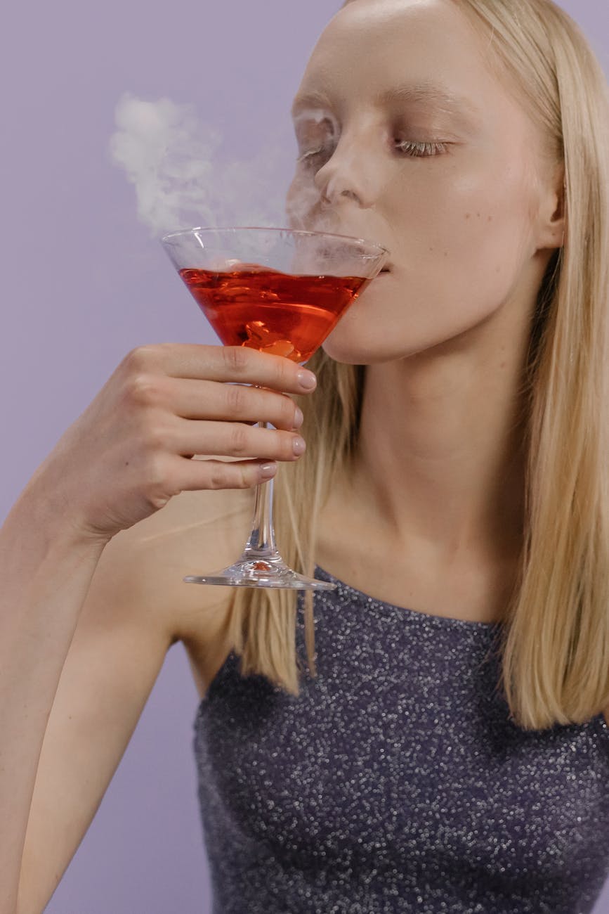 woman in gray tank top drinking red liquid from clear drinking glass